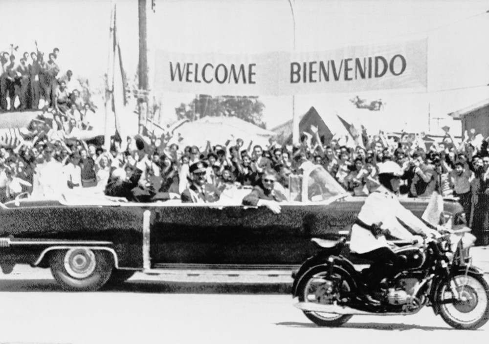On this date in 1960: President Dwight D. Eisenhower waves to the crowd from car as his motorcade passes a banner welcoming him in English and Spanish in Santiago, Chile. 