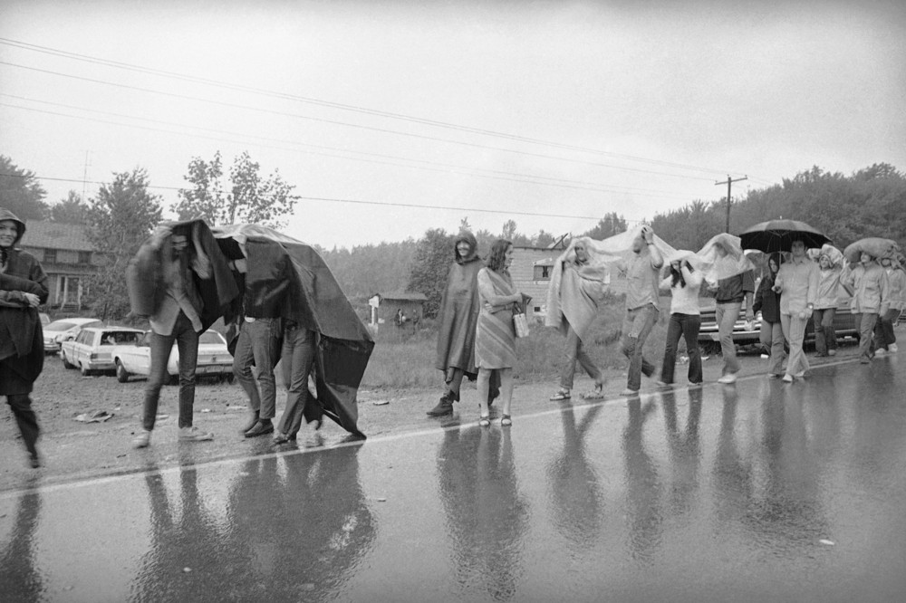 On this date in 1969: Woodstock attendees walk along the wet highway leading from Bethel, New York as they leave the Woodstock Music and Art Festival. Two hundred thousand persons spent a rainy night at the festival.