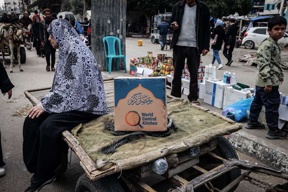 A Palestinian woman sits on a cart next to a box of food rations provided by World Central Kitchen.