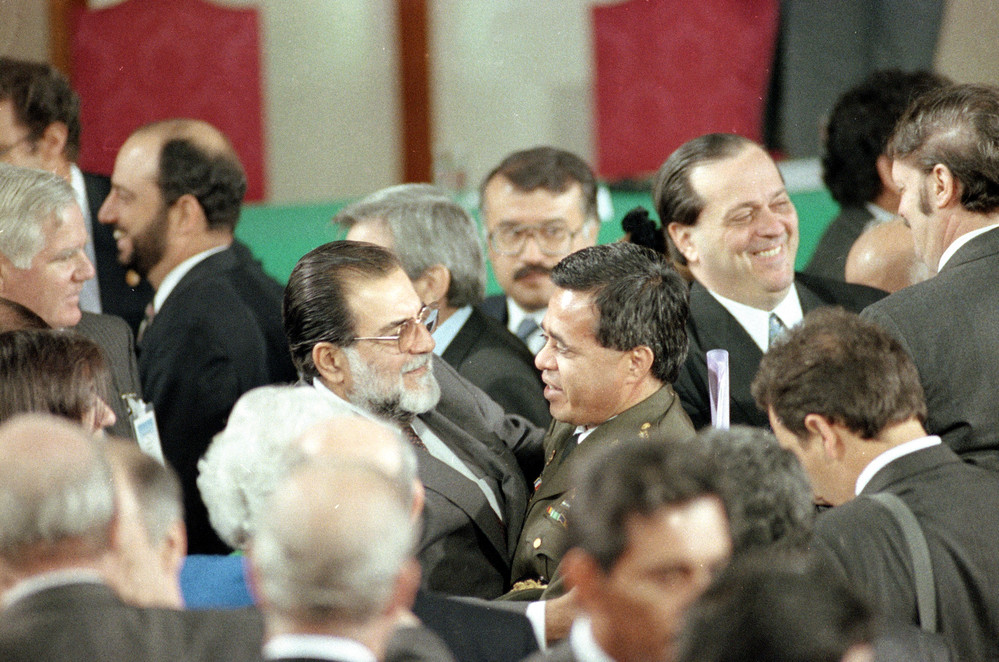 On this date in 1992: The El Salvadoran Peace Accords are signed at Chapultepec Castle in Mexico City between the government of El Salvador and the FMLN guerrilla leaders, officially ending the country's 12-year civil war. Pictured is General Mauricio Ernesto Vargas (center right) of the Salvadoran armed forces embracing Schafik Handel (left) commander of the FMLN.