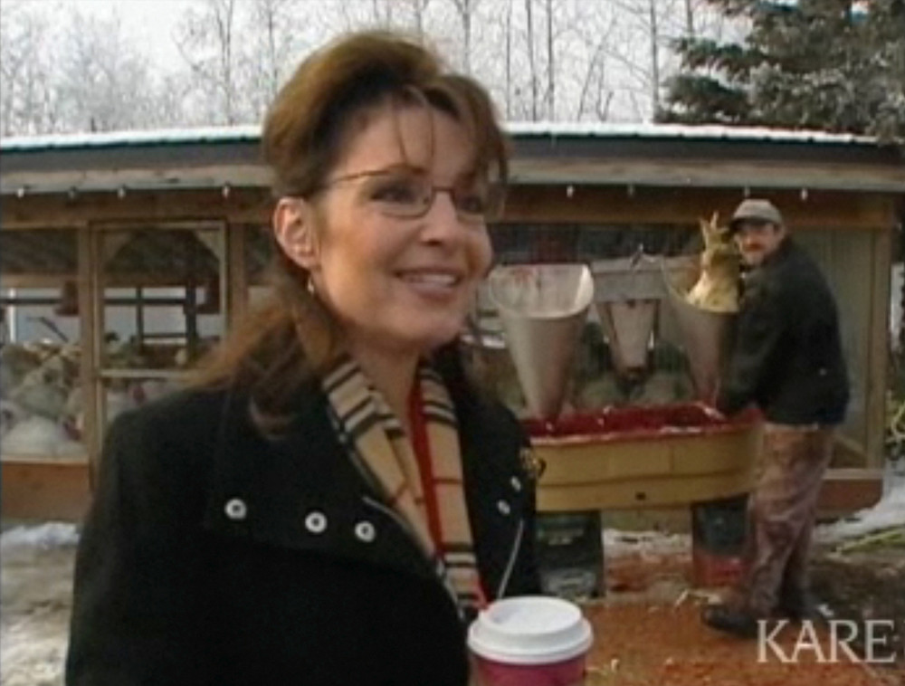 In this image rendered from video, Alaska Gov. Sarah Palin speaks during an interview on Nov. 20, 2008 at Triple D Farm & Hatchery outside Wasilla, Alaska. As Palin answered questions, cameras from the Anchorage Daily News and others showed the bloody work of an employee, right, slaughtering birds behind the former Republican vice presidential candidate.