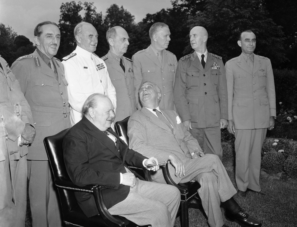 On this date in 1943: British Prime Minister Winston Churchill, left, and U.S. President Franklin D. Roosevelt meet at the White House to discuss the ongoing war effort. They are surrounded by advisors standing behind them. 
