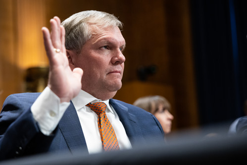Norfolk Southern President and CEO Alan Shaw holding his hand up while sitting at a table in a hearing room.
