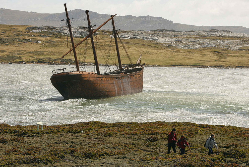Visitors walk near the wreck of a boat