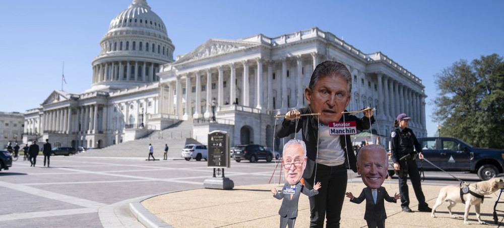 A protester holding up representations of Senator Joe Manchin, House Speaker Chuck Schumer, and President Joe Biden at the Capitol in Washington, D.C. (photo: Sarah Silbiger/Bloomberg)