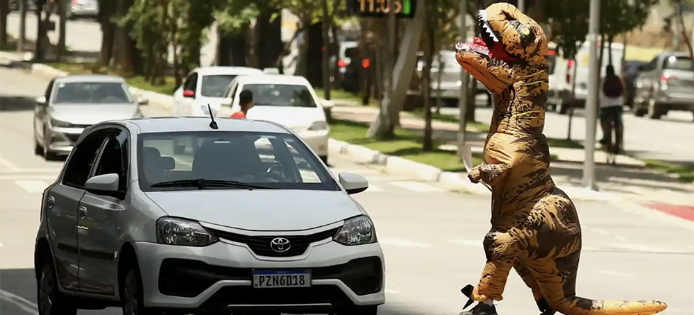 A demonstrator dressed as a dinosaur protests the BTG Pactual Bank, which does business with companies that explore fossil fuels in the Amazon region. (photo: Carla Carniel/Reuters)