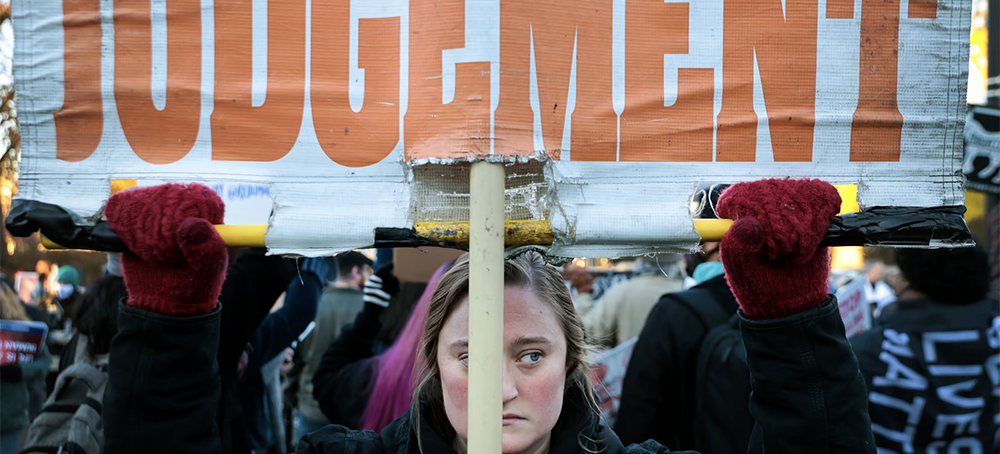 A photo of a protester holding a sign that reads 'Judgement' in orange letters on a white background. (photo: Chip Somodevilla/Getty Images)