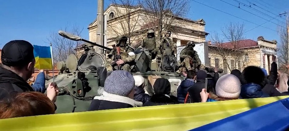 Pro-Ukrainian protesters pass Russian soldiers during a demonstration in Kherson. (photo: BBC)