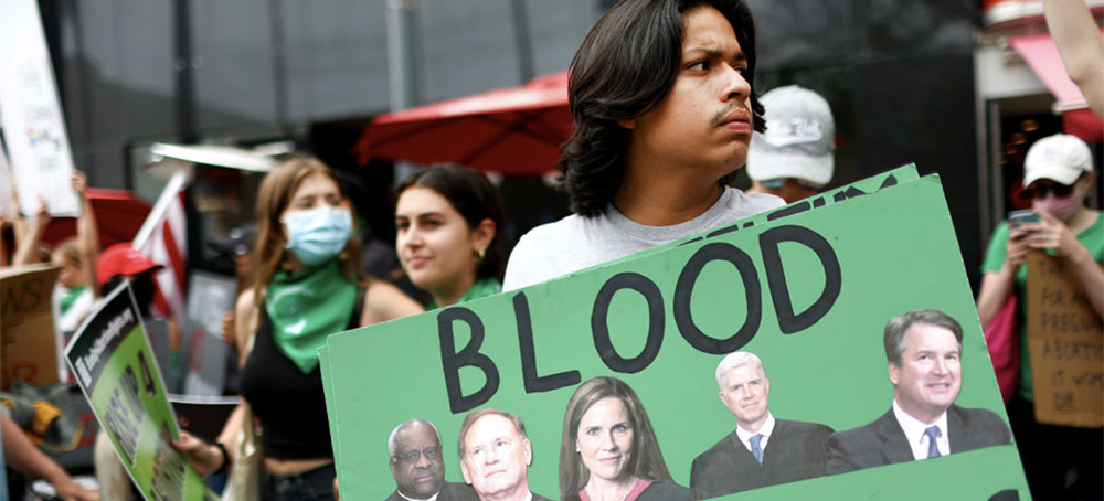 An abortion rights activist holds a sign depicting Supreme Court justices Clarence Thomas, Samuel A. Alito Jr, Amy Coney Barrett, Neil M. Gorsuch, and Brett M. Kavanaugh during a demonstration outside a Planned Parenthood clinic as they safeguard the clinic from a possible protest by a far-right group on July 16, 2022, in Santa Monica, California. (photo: Mario Tama/Getty Images)