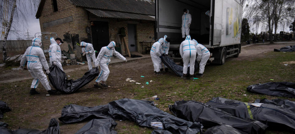 Volunteers load bodies of civilians killed in Bucha onto a truck to be taken to a morgue for investigation, in the outskirts of Kyiv, Ukraine, Tuesday, April 12, 2022. (photo: AP)