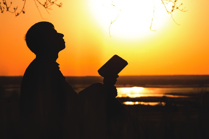 A person holding a Bible and looking up to the sky.