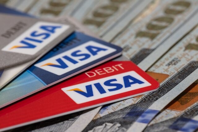 Miami, Florida - June 3, 2020: Red, blue, and silver Visa debit cards on hundred dollar bills. Some cards and bills are in soft focus. Business concept. Angled, Close-up shot. Illustrative editorial.